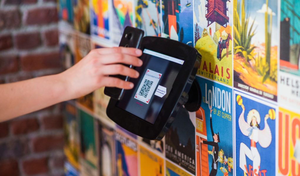 Guest holding a smartphone to scan a QR code displayed on a hotel lobby tablet